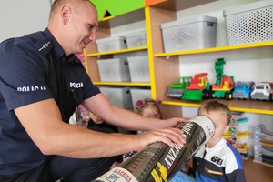 Mundurowy tłumaczy dzieciom zasadę działania odblasków przy użyciu magicznej tuby