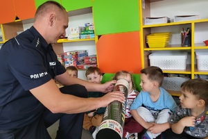 Mundurowy tłumaczy dzieciom zasadę działania odblasków przy użyciu magicznej tuby