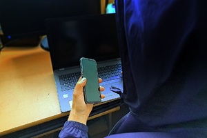 Mężczyzna z kapturem na głowie trzyma telefon w ręku