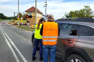 Policjantka i przedstawiciel PKP PLK wręczają ulotki i rozmawiają o bezpieczeństwie na przejeździe kolejowym
