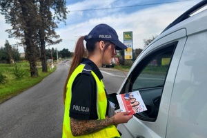 Policjantka i przedstawiciel PKP PLK wręczają ulotki i rozmawiają o bezpieczeństwie na przejeździe kolejowym