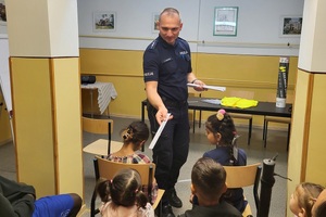 Policjant rozmawia z cudzoziemcami oraz rozdaje  elementy odblaskowe